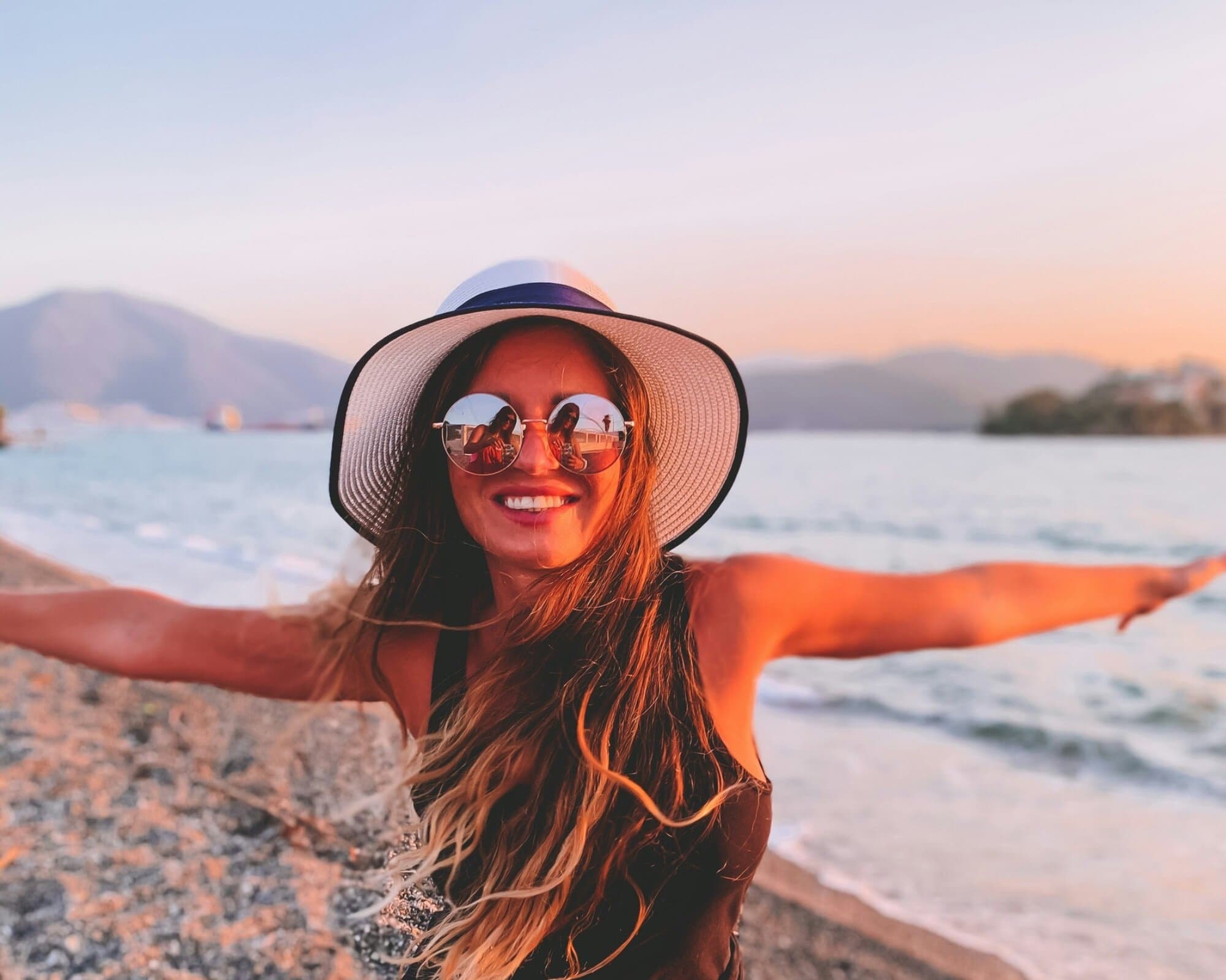 A traveller in a sun hat at the water's edge on a Greek beach at sunset