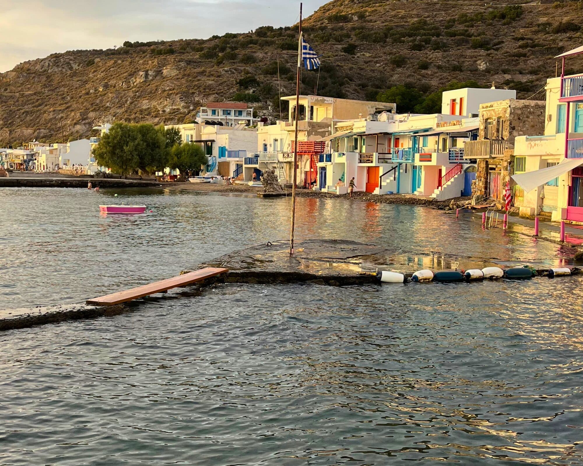Colourful fishermen's boathouses lining the waterfront of a Milos fishing village at sunset, seen from the water